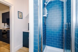 A modern bathroom with blue tiles, a glass shower enclosure, and a visible kitchen area with dark cabinets. - Spacious 4 Bed Home in Crewe Perfect for Groups (Crewe)