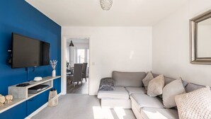 A living room with a TV, sofa, and a blue accent wall. - Modern 2 Bedroom Home in Swansea Near Stadium (Swansea)