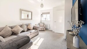 A modern living room with a grey sofa, a small armchair, a white vase with branches, and a large mirror on the wall. - Modern 2 Bedroom Home in Swansea Near Stadium (Swansea)