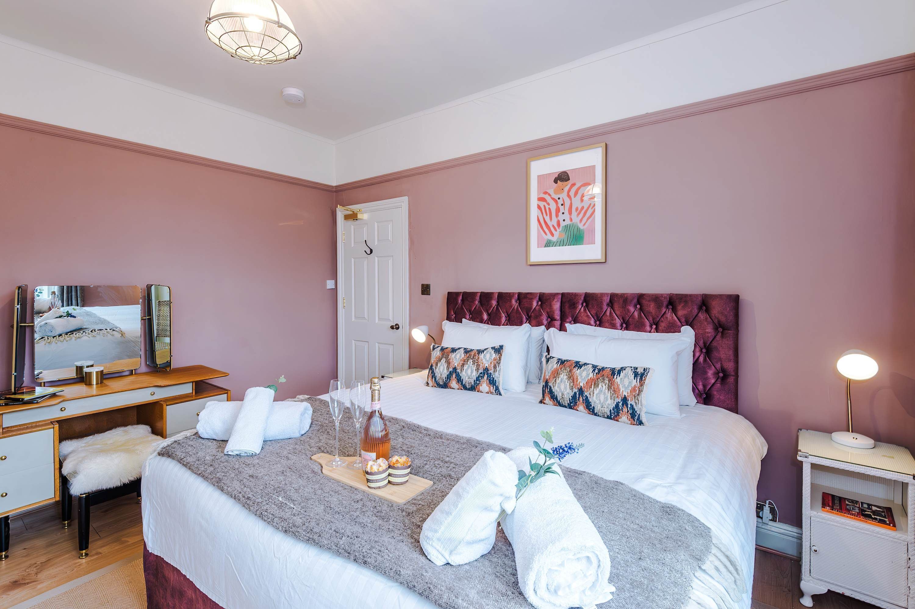 A bedroom with a bed, bedside table, lamp, and a mirror.