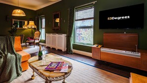 Una sala de estar con un sofá, una mesa de centro con libros, una televisión y un ventanal con cortinas.