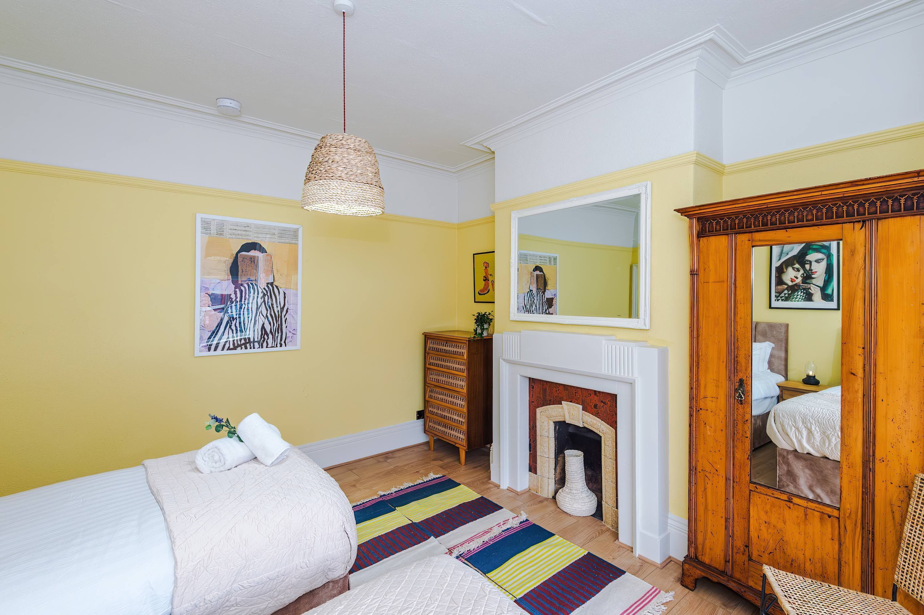 Un dormitorio con cama, tocador, espejo, chimenea y lámpara colgante.
