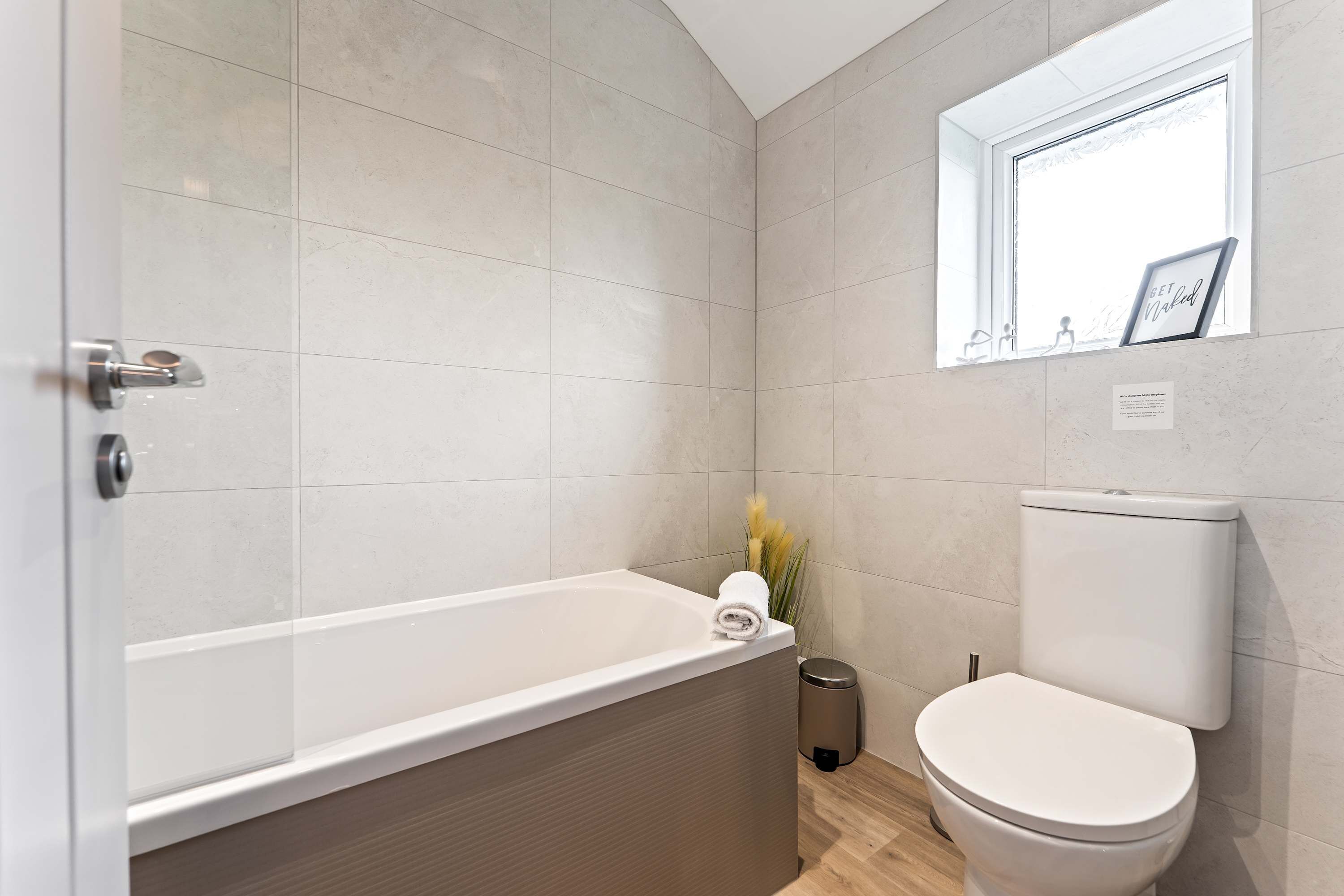 Een moderne badkamer met een badkuip, toilet en raam met een fotolijst.