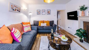 A living room with a sofa, a coffee table with a bottle and glasses, a TV, and framed pictures on the wall. - Spacious 3 Bed Perfect for Families and Groups (Nantwich)
