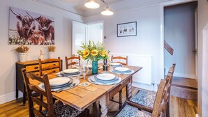 A dining area with a wooden table set for six, chairs, a vase with sunflowers, and artwork on the walls. - Spacious 3 Bed Perfect for Families and Groups (Nantwich)