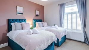 A bedroom with two beds, a large window with curtains, and artwork on the wall. - Spacious 3 Bed Perfect for Families and Groups (Nantwich)