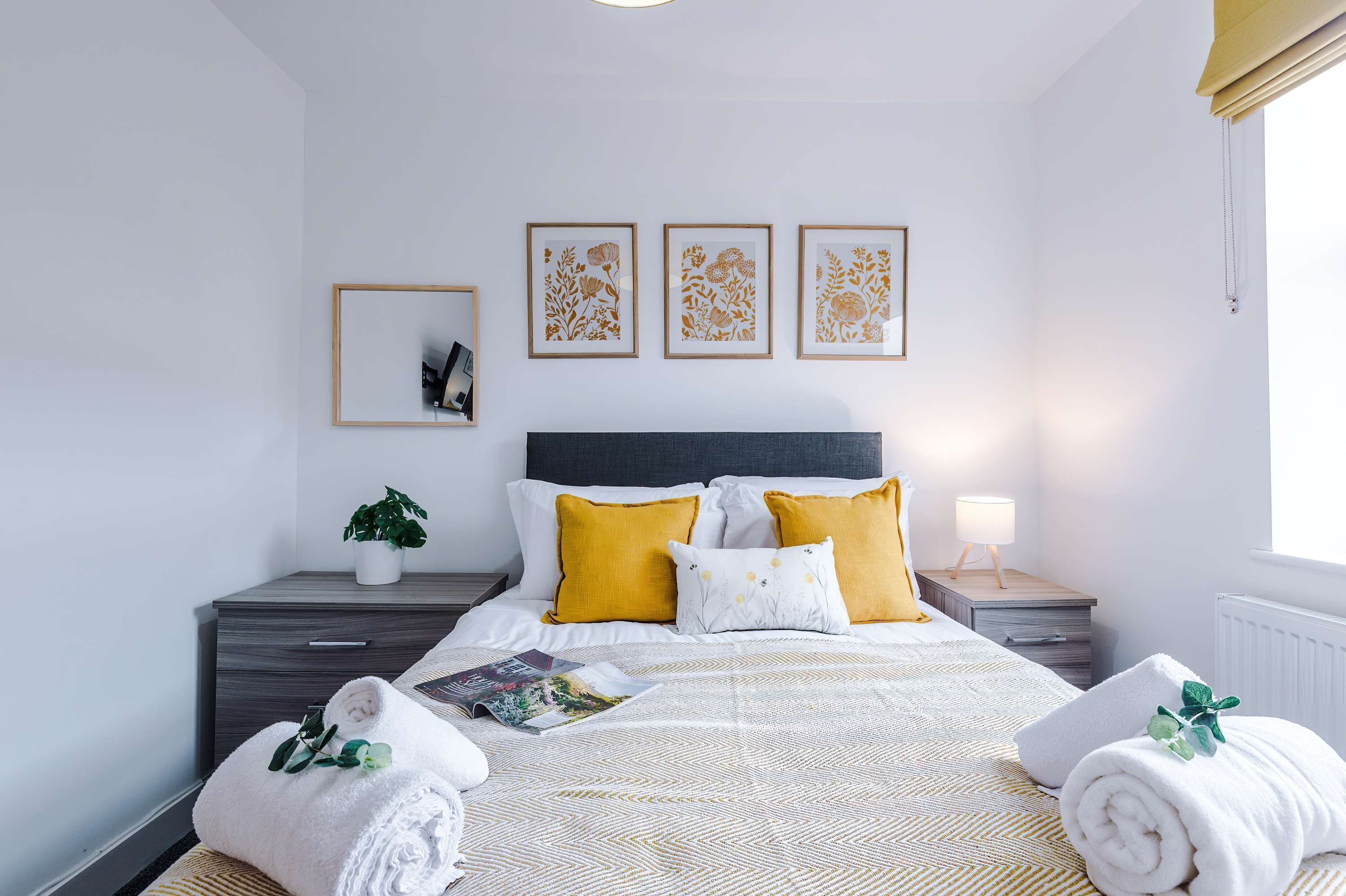 Une chambre d’hôtel bien rangée, avec un lit, des tables de chevet, une petite table, une plante en pot et des œuvres d’art accrochées au mur.