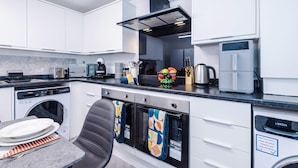 Cozinha moderna com armários brancos, lava-louças embutida, máquina de café e micro-ondas.