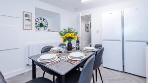 Uma sala de jantar moderna com uma mesa posta para quatro pessoas, um relógio e uma geladeira.