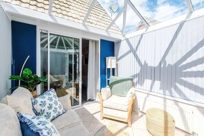 Een zonnig terras met een bank, een stoel, een lamp en een plant in een pot.