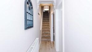 A narrow hallway with a wooden staircase, a radiator, and a window with a decorative frame. - Perfect Modern 4 Bed in Crewe Great for Business (Crewe)