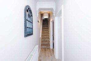 A narrow hallway with a wooden staircase, a radiator, and a window with a decorative frame. - Perfect Modern 4 Bed in Crewe Great for Business (Crewe)