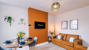 A modern living room with a round dining table, a sofa, and a TV mounted on the wall. - Perfect Modern 4 Bed in Crewe Great for Business (Crewe)