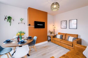 A modern living room with a round dining table, a sofa, and a TV mounted on the wall. - Perfect Modern 4 Bed in Crewe Great for Business (Crewe)