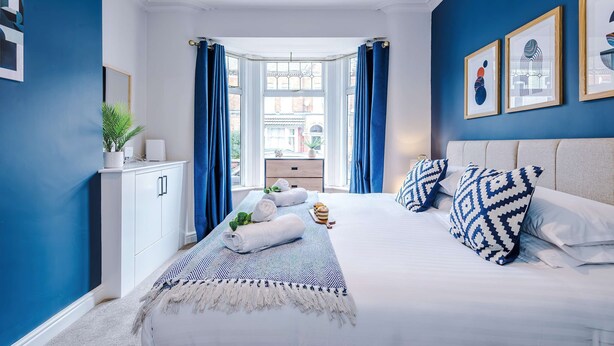 A bedroom with a large bed, a nightstand, a dresser, and a window with curtains. - Perfect Modern 4 Bed in Crewe Great for Business (Crewe)