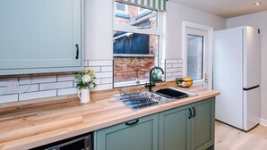 A kitchen with a wooden countertop, a sink, a window with a view of a brick building, and a white refrigerator. - Perfect Modern 4 Bed in Crewe Great for Business (Crewe)