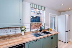 A kitchen with a wooden countertop, a sink, a window with a view of a brick building, and a white refrigerator. - Perfect Modern 4 Bed in Crewe Great for Business (Crewe)