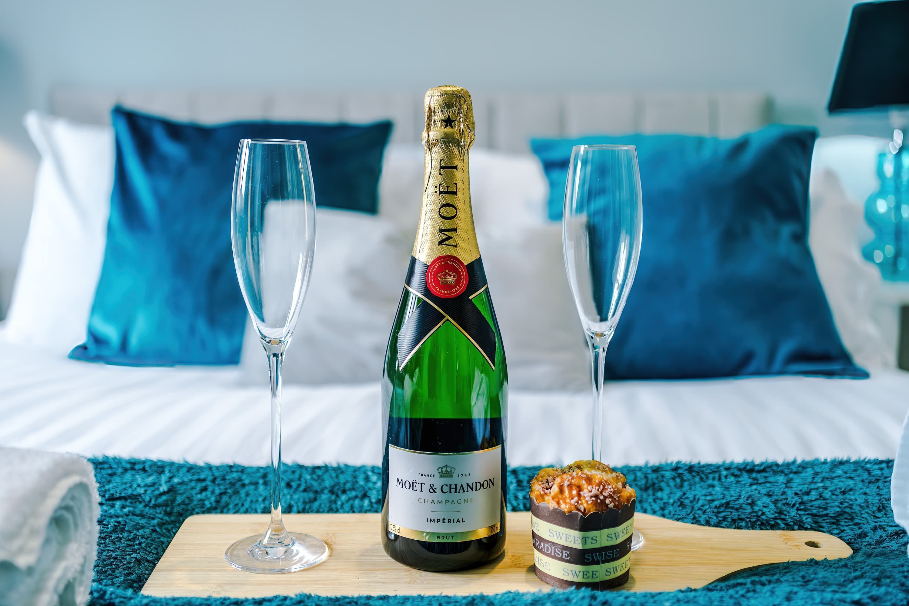 En flaske Moët & Chandon champagne, to glas og en dessert på en træplade i et hotelværelse.