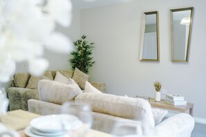 A living room with a sofa, a coffee table, and two wall-mounted mirrors. - Spacious 3 Bed in Northwich Perfect for Groups (Northwich)