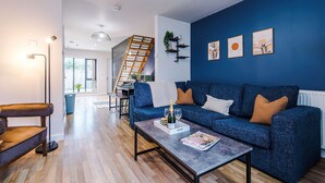Ein modernes Wohnzimmer mit einem blauen Sofa, einem Couchtisch mit einer Zeitschrift, einer Stehlampe und einer Treppe, die in einen anderen Raum führt.