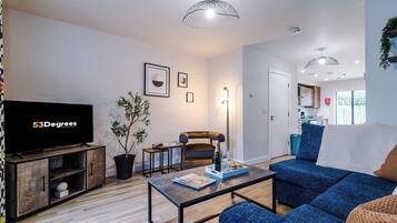A modern living room with a flat-screen TV, a sofa, a coffee table, and a dining area.