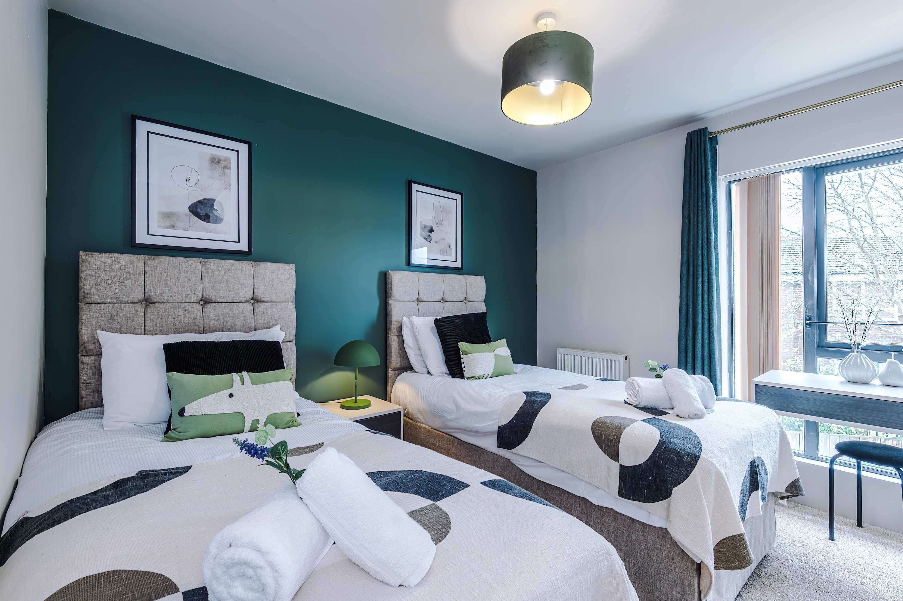 A hotel room with two beds, a window with curtains, a desk, and a chair.