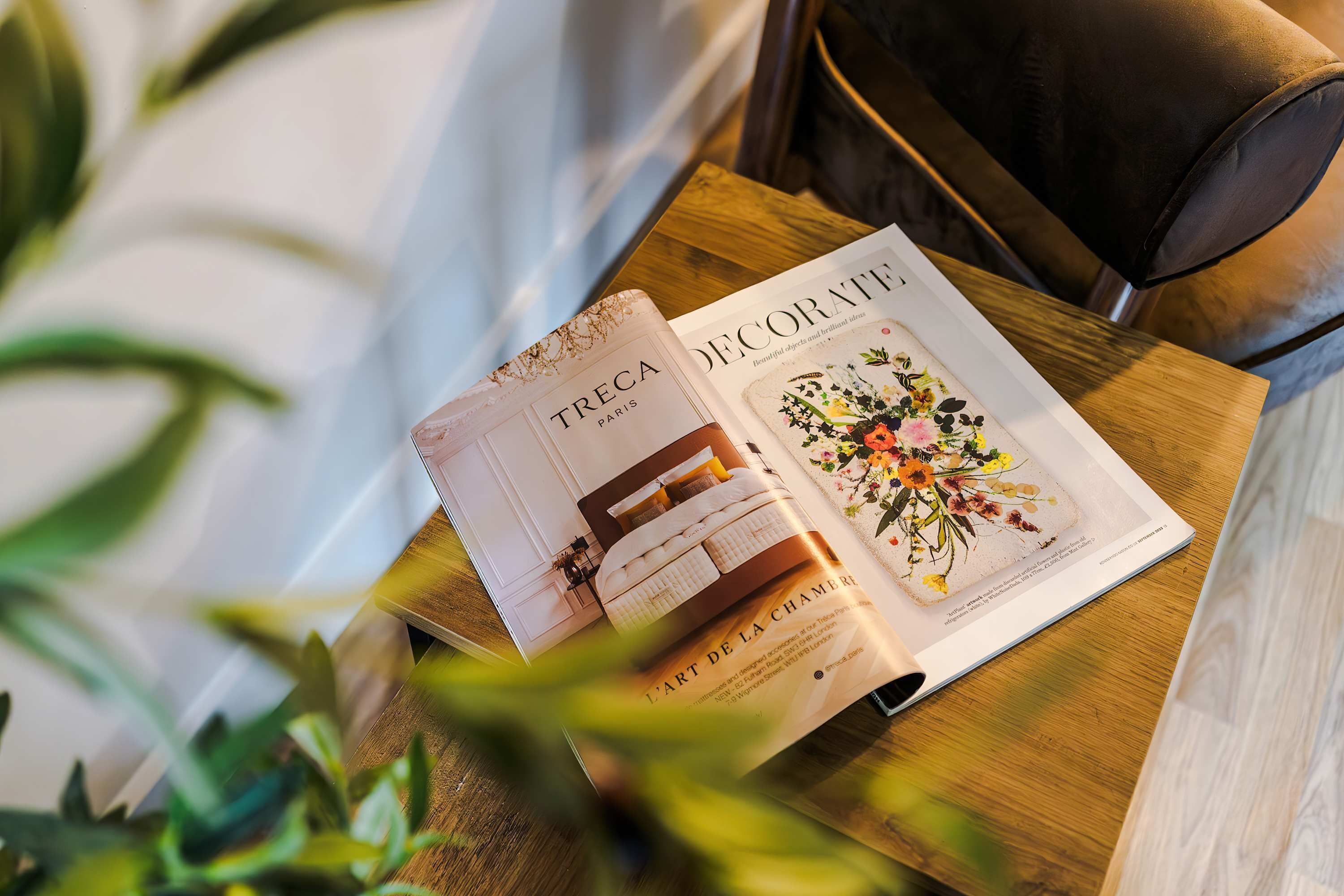A magazine on a wooden table with a plant in the foreground.