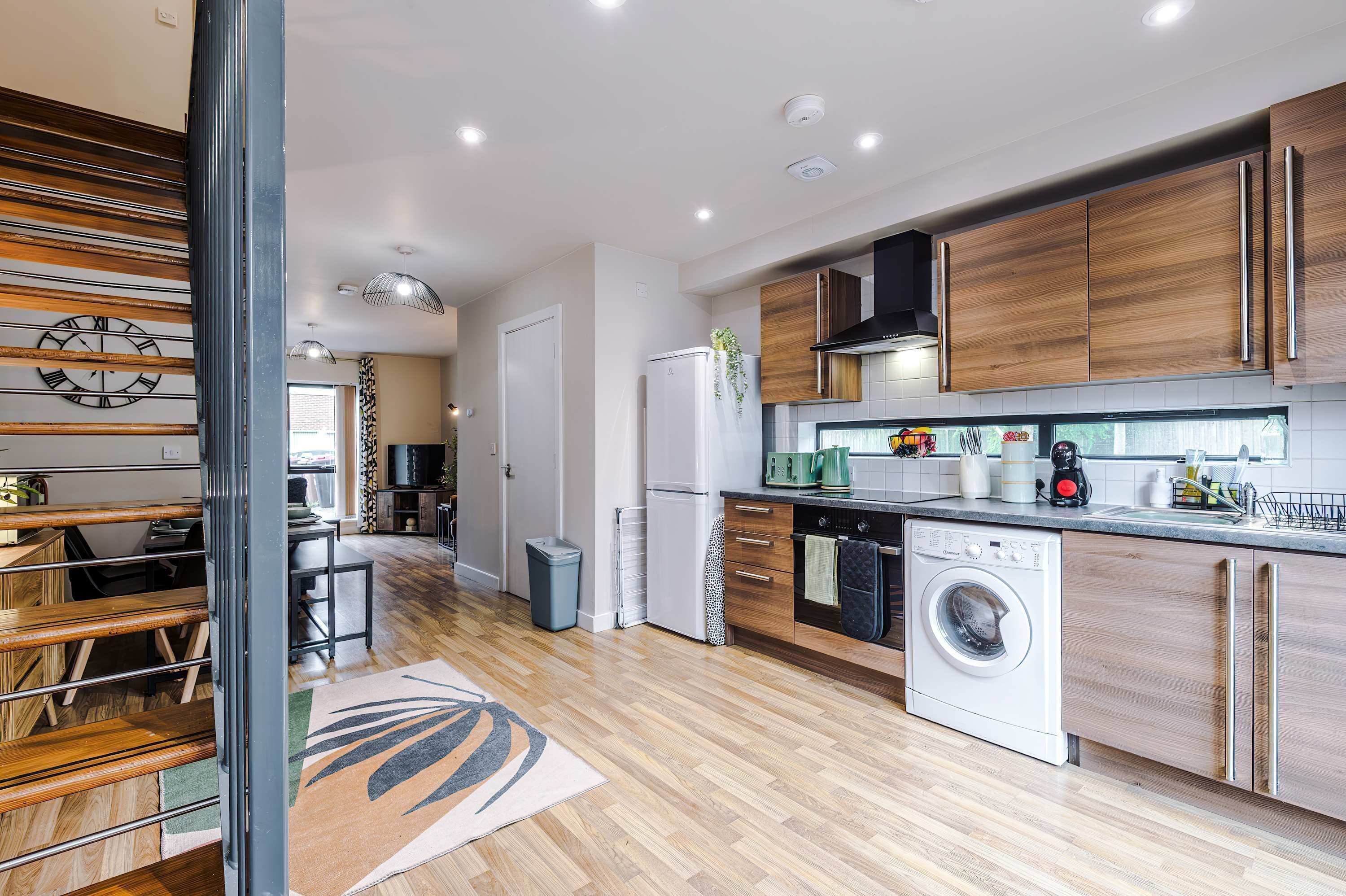 A modern kitchen with wooden cabinets, a built-in washing machine, and a dining area with a wooden table and chairs.