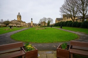 A park with a central lawn, benches, a statue, and a building with a clock tower. - Homely 2 Bed Close to Leeds City Center Sleeps 3 (Batley)
