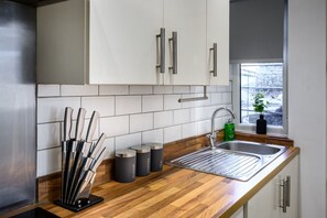 A kitchen with white cabinets, a stainless steel sink, and a window with a view of a snowy landscape. - Homely 2 Bed Close to Leeds City Center Sleeps 3 (Batley)