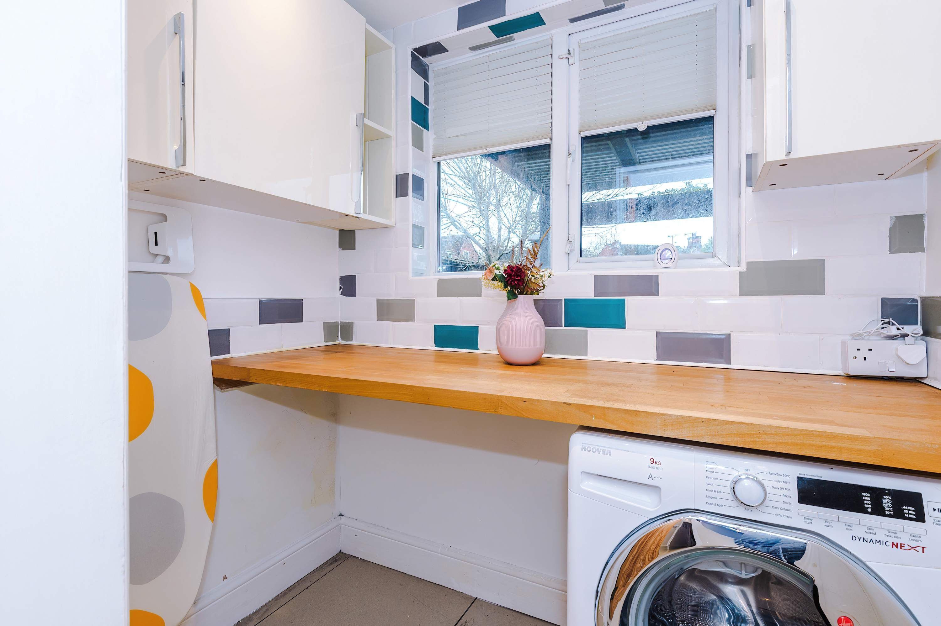 A compact kitchen with a wooden countertop, a washing machine, and a window with blinds.