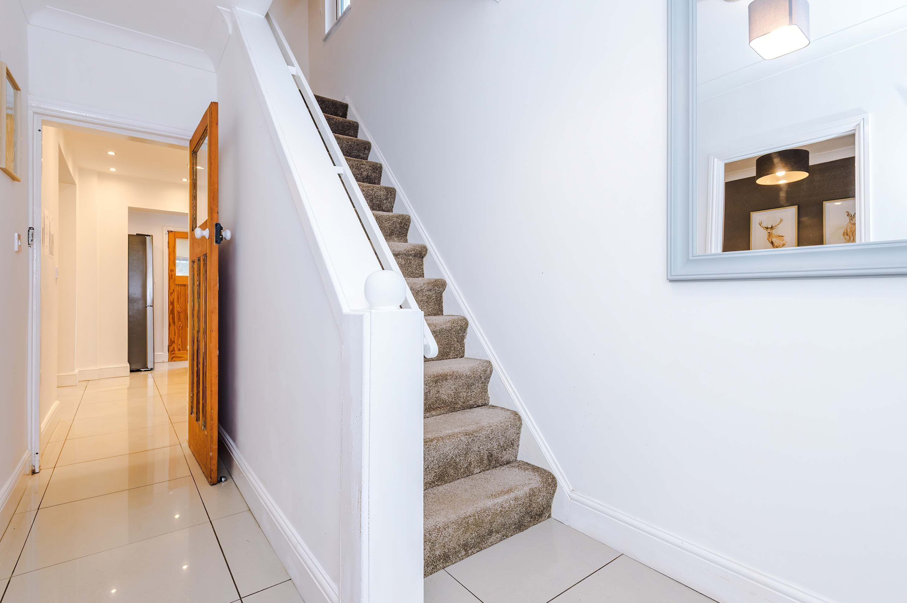 Una escalera con peldaños alfombrados y barandilla blanca, que conduce a un cuarto con una puerta y un accesorio de luz en la pared.