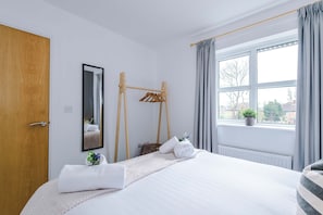 A hotel room with a bed, a wooden drying rack, a mirror, a window with curtains, and a radiator. - Stunning 1 Bed Flat Perfect for Business in Crewe (Crewe)