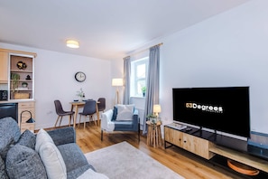 A modern living room with a flat-screen TV, a sofa, a dining area, and a kitchen. - Stunning 1 Bed Flat Perfect for Business in Crewe (Crewe)