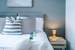 A neatly made bed with striped and patterned pillows, a bedside lamp, and a framed picture on the wall. - Stunning 1 Bed Flat Perfect for Business in Crewe (Crewe)