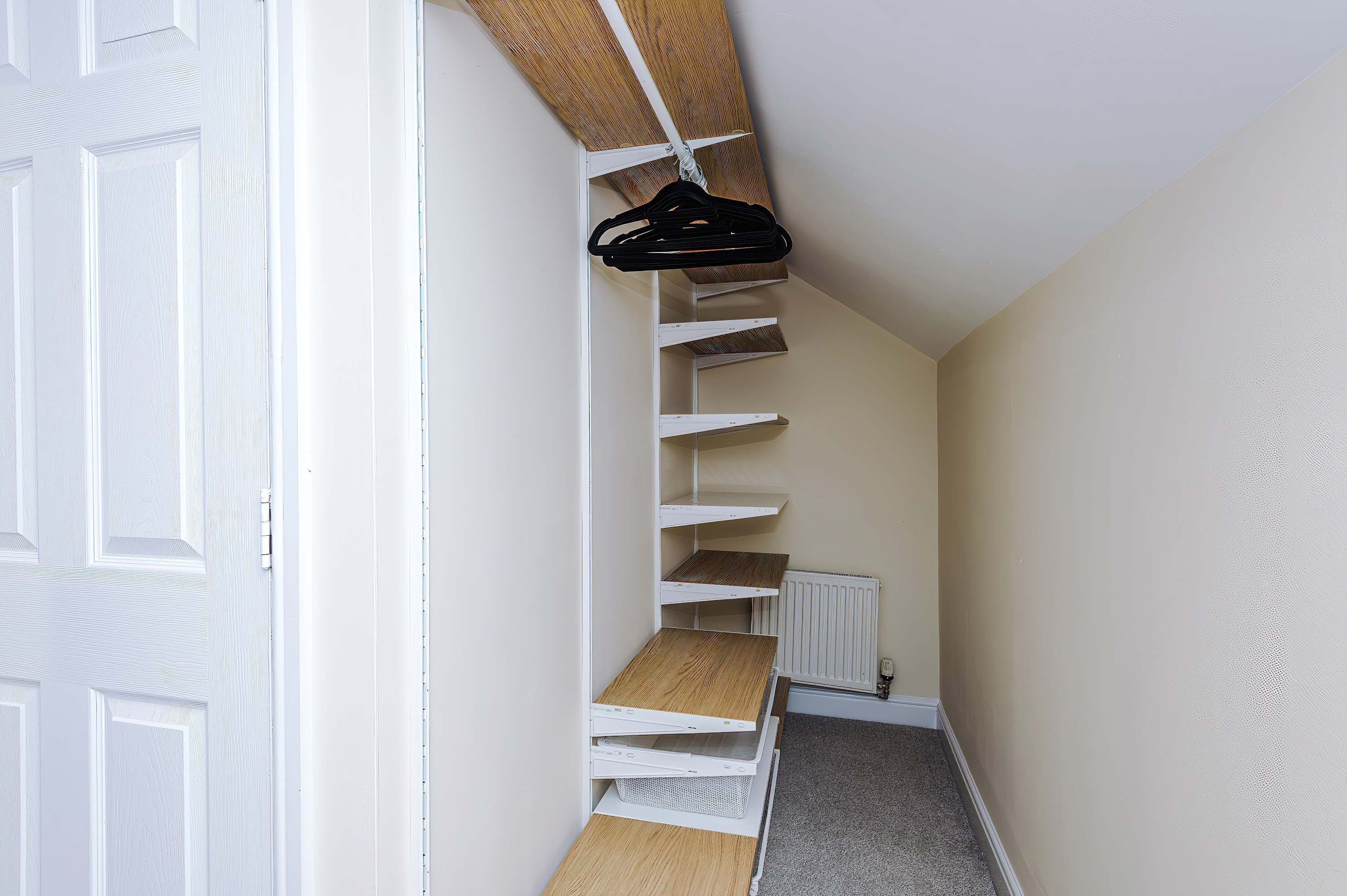 A narrow hallway with a white door on the left, a radiator on the right, and a black hanger on a white shelf.