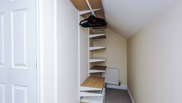 A narrow hallway with a white door on the left, a radiator on the right, and a black hanger on a white shelf.