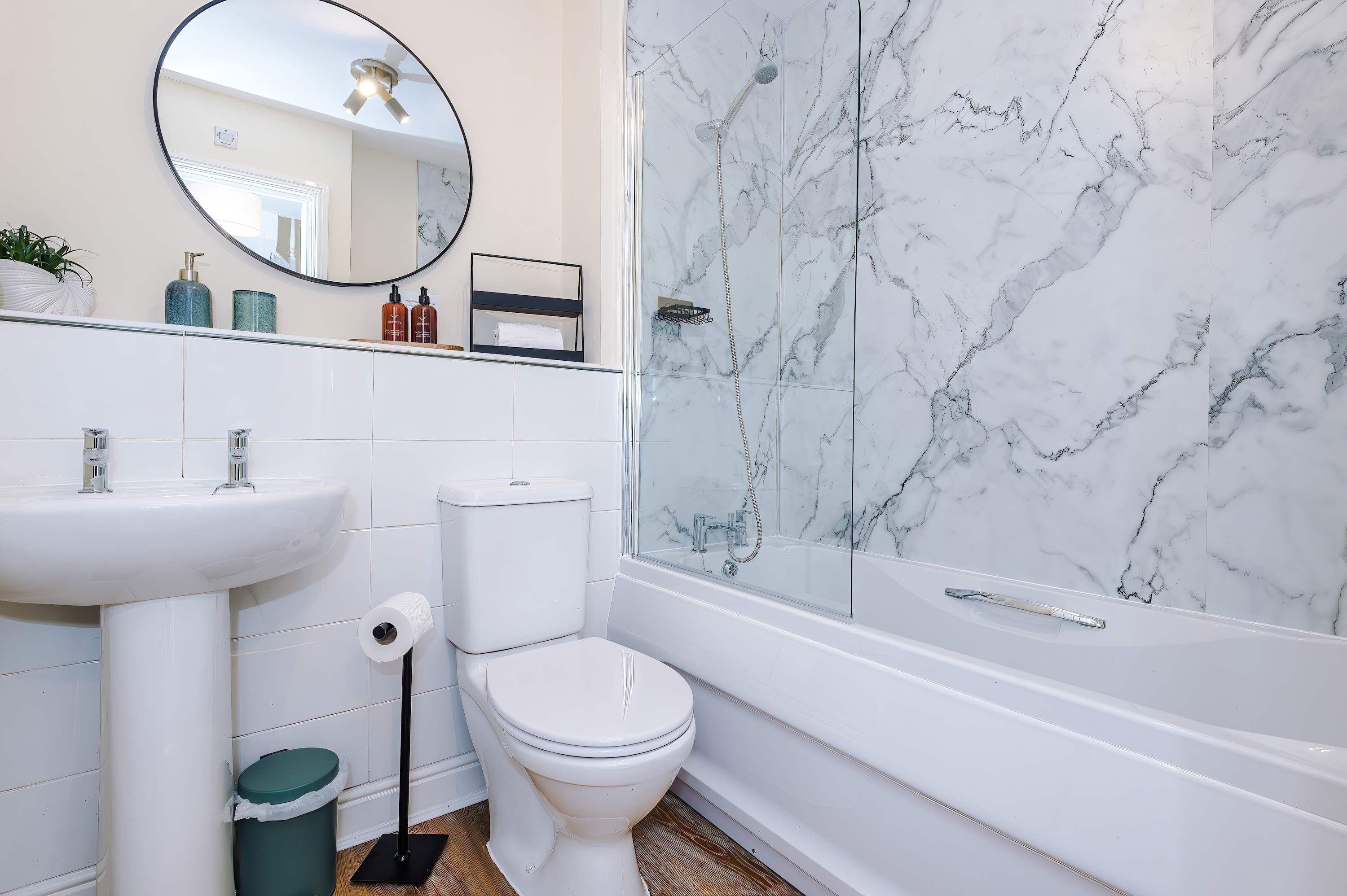 Une salle de bain avec un lavabo blanc, des toilettes et une douche, le tout agrémenté de murs en marbre.