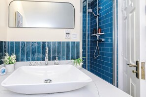 A bathroom with a white sink, a mirror, a shower with blue tiles, and a door with a brass handle. - Spacious Modern 4 Bed in Northwich Free Parking (Northwich)