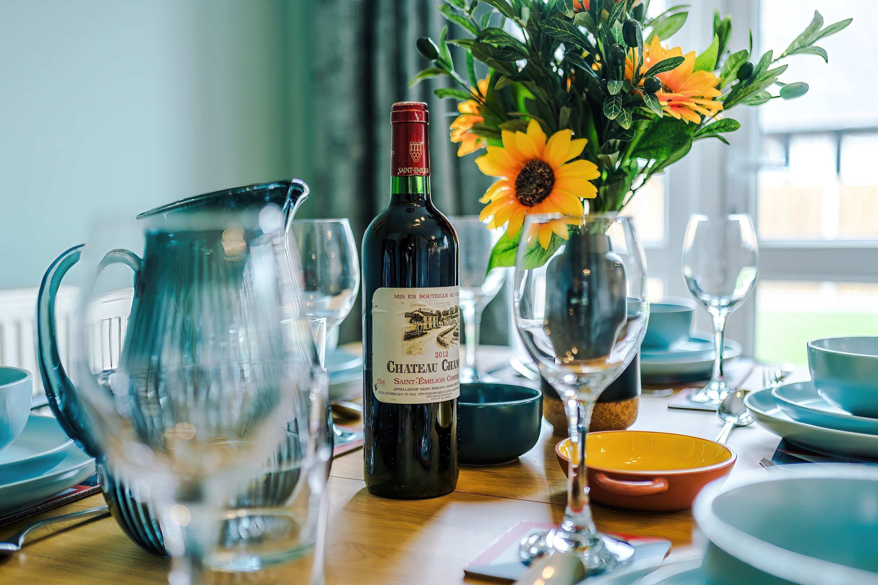Une table dressée avec des verres à vin, une bouteille de vin et un vase rempli de fleurs.