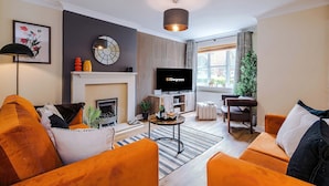 Ein modernes Wohnzimmer mit Kamin, orangefarbenen Sofas, einem Flachbildfernseher und einem großen Fenster.