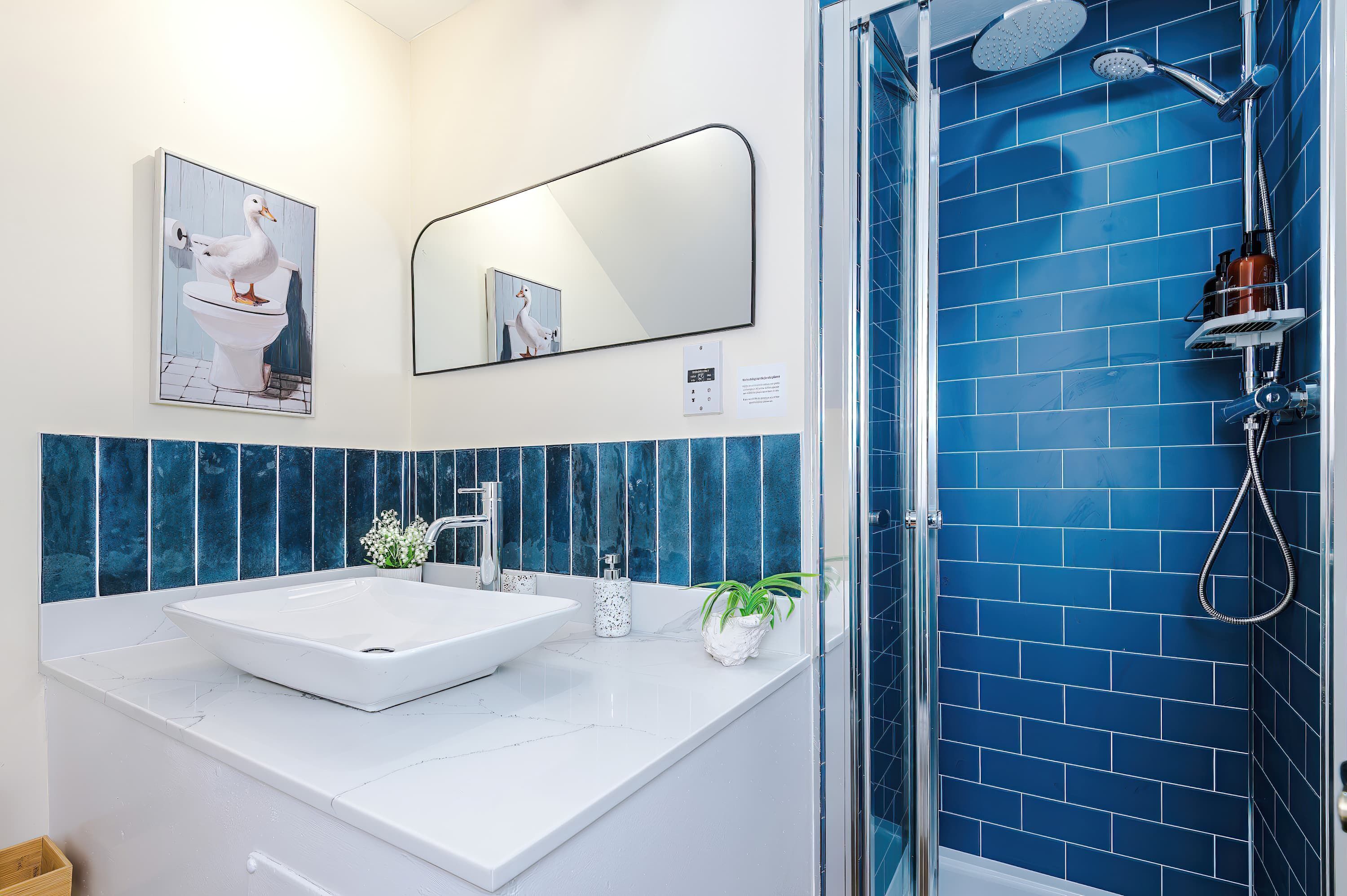 A bathroom with a white sink, a mirror, a shower with blue tiles, and a wall-mounted toilet paper holder.