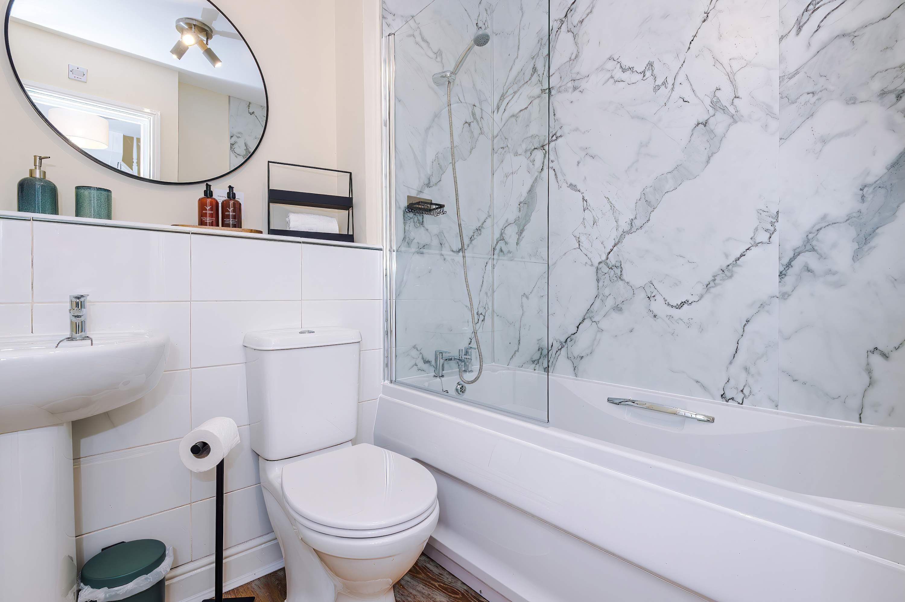 A bathroom with a white toilet, a sink, a shower with a glass door, and a marble wall.
