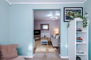 Ein Wohnzimmer mit einer Couch, einem Couchtisch, einem Bücherregal, einem Fernseher und einem gerahmten Bild an der Wand.