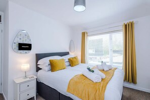 Ein Hotelzimmer mit Bett, Nachttisch, Lampe, Wand-Fernseher und einem Fenster mit Vorhängen.