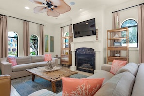 A living room with a sofa, coffee table, fireplace, TV, and shelves. - 6 Bedroom Home with Pool 10 minute Walk To Beach (Miramar Beach)