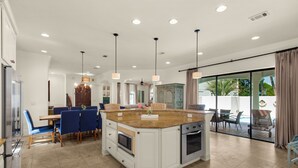 Een ruime keuken met een groot eiland, moderne apparaten en een eethoek met blauwe stoelen.