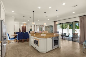 A spacious kitchen with a large island, modern appliances, and a dining area with blue chairs. - 6 Bedroom Home with Pool 10 minute Walk To Beach (Miramar Beach)
