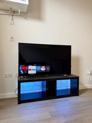 Un televisor de pantalla plana sobre un mueble de entretenimiento negro con frentes de vidrio, frente a una pared lisa.