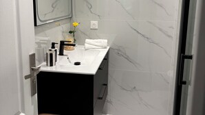 Un bagno moderno con una parete in marmo, un ampio specchio, un lavandino bianco e un piccolo sgabello.